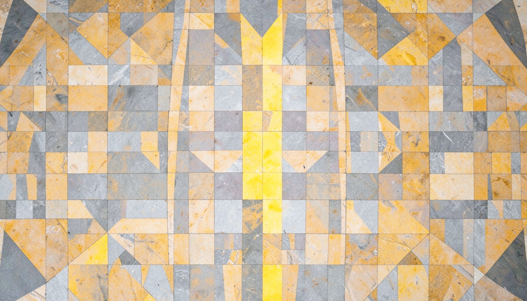 Symmetrical overhead view of a patterned stone plaza in muted gray and ochre with sharp geometric lines